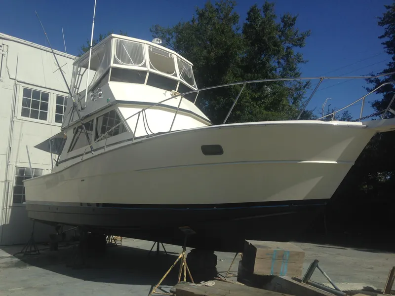 Slide: The Image of 1986 Viking 35 Sportfish boat on dry dock, white exterior, near building and trees. - 3