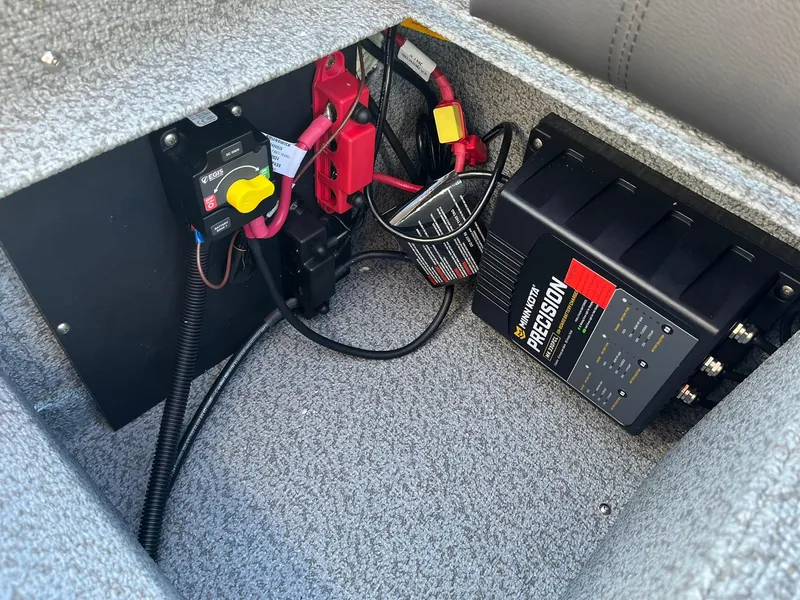 Slide: The Image of 2025 Lund 1775 Impact XS Sport battery compartment with wiring and charger. - 27