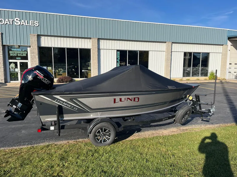 Slide: The Image of 2025 Lund 1775 Impact XS Sport boat with cover, parked outside dealership. - 29