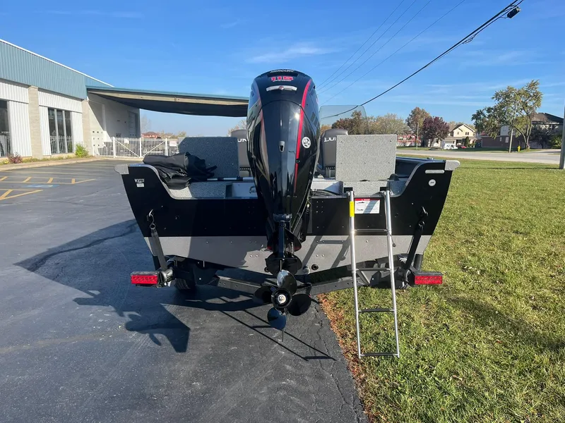 Slide: The Image of 2025 Lund 1775 Impact XS SS boat, rear view with motor and ladder, parked outdoors. - 2