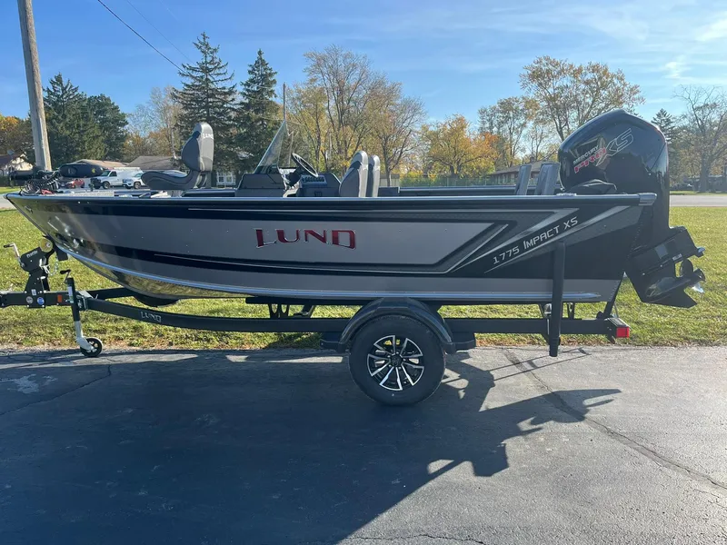 Slide: The Image of 2025 Lund 1775 Impact XS SS fishing boat on trailer, parked outdoors. - 3