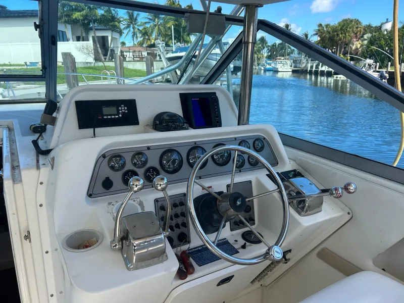 Slide: The Image of 1999 Wellcraft 330 Coastal boat helm with gauges and controls, docked by a scenic marina. - 15