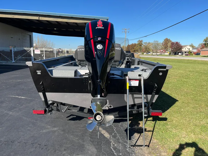 Slide: The Image of 2025 Lund 1875 Impact XS SS boat with outboard motor, parked outdoors. - 2