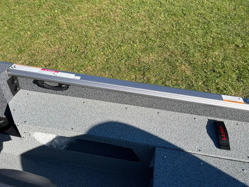 Slide: The Image of 2025 Lund 1875 Impact XS SS boat interior with gray flooring and green grass background. - 21