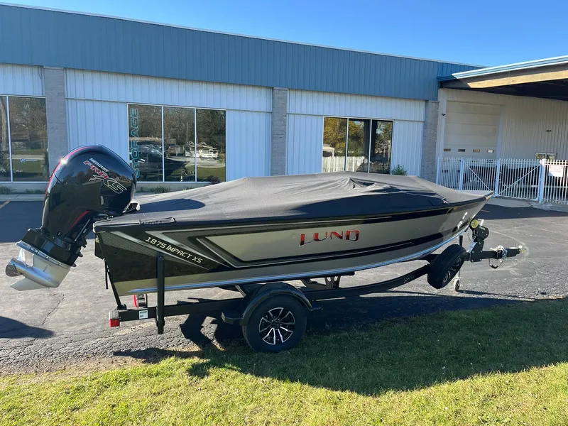 Slide: The Image of 2025 Lund 1875 Impact XS SS boat with cover on trailer, parked outdoors. - 25