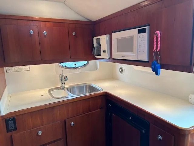 Slide: The Image of 2000 Tiara Yachts 3700 Open kitchen with wood cabinets, sink, microwave, and porthole. - 32