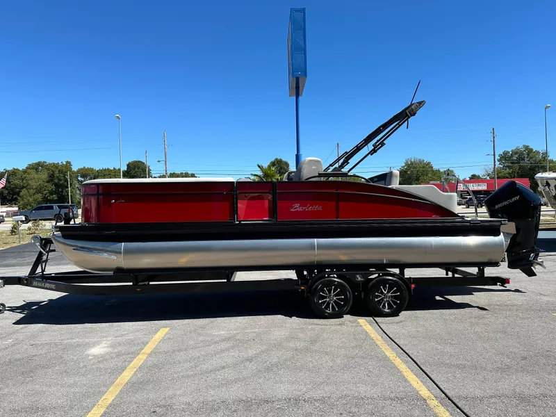 Slide: The Image of 2025 Barletta A24UC pontoon boat on trailer, red and silver design, parked outdoors. - 5
