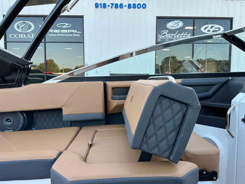 Slide: The Image of 2024 Cobalt R6 boat interior with tan and black seating, dealership in background. - 16