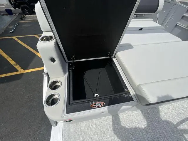 Slide: The Image of 2024 Harris 230CX boat storage compartment with cup holders, open lid, and gray seating. - 14