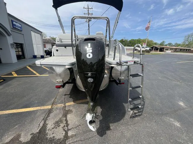 Slide: The Image of 2024 Harris 230CX pontoon boat with 150 HP engine, parked outdoors. - 22