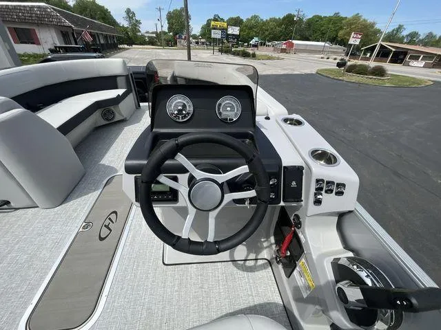 Slide: The Image of 2024 Harris 230CX boat dashboard with steering wheel and gauges, parked outdoors. - 3