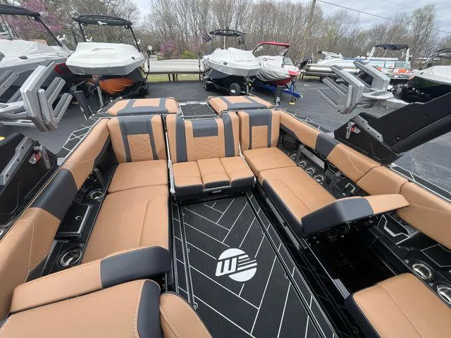 Slide: The Image of 2024 Malibu 23LSV boat interior with tan and black seating, docked among other boats. - 18