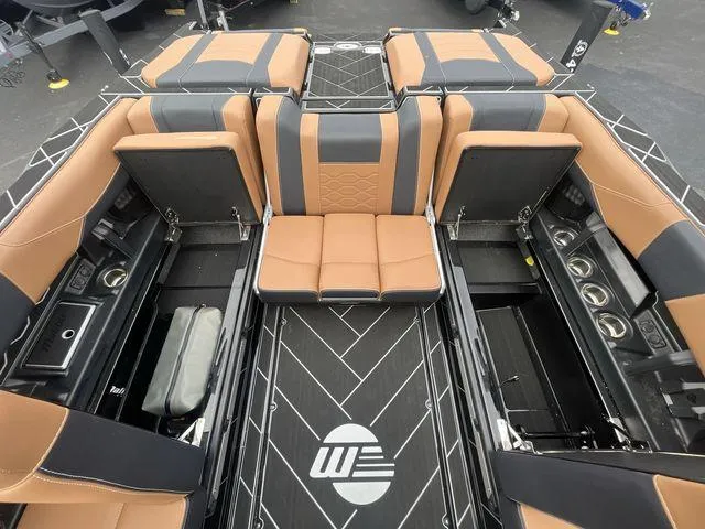 Slide: The Image of 2024 Malibu 23LSV boat interior with tan and black seating, cup holders, and storage compartments. - 6