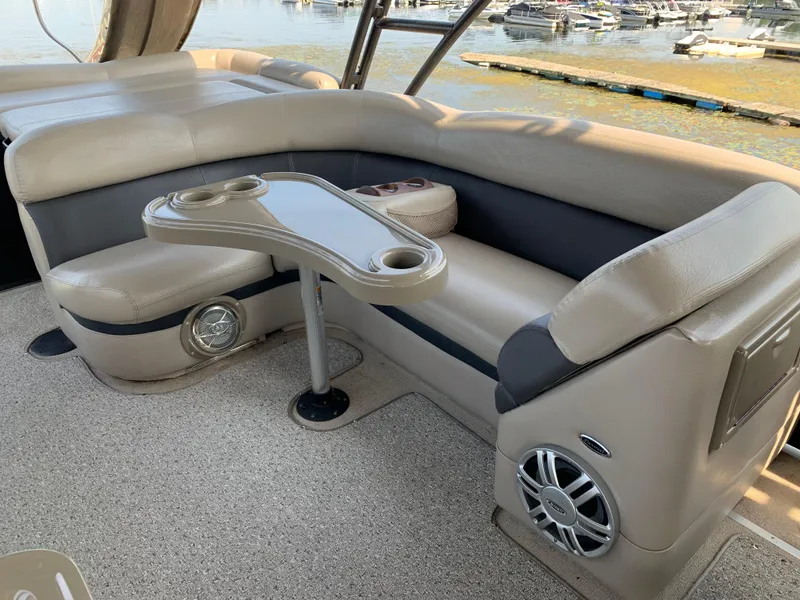Slide: The Image of 2013 Premier 310 Boundary Waters Sky Dek interior with beige seating and table, docked by the water. - 16
