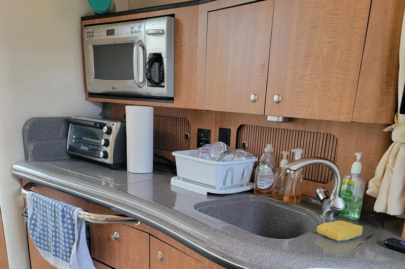 Slide: The Image of 2006 Sea Ray 320 Sundancer kitchen with microwave, sink, and wooden cabinets. - 35