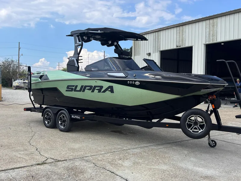 Slide: The Image of 2023 Supra SL 450 boat on trailer, parked outside a warehouse. - 2