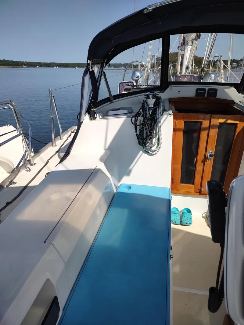 Slide: The Image of 2007 Outbound 46 sailboat cockpit with blue mat, wooden door, and calm water view. - 21