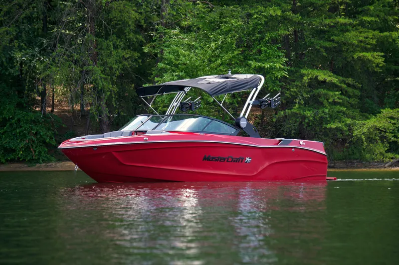 Slide: The Image of 2024 MasterCraft XT23 boat in vibrant red on a serene lake. - 2