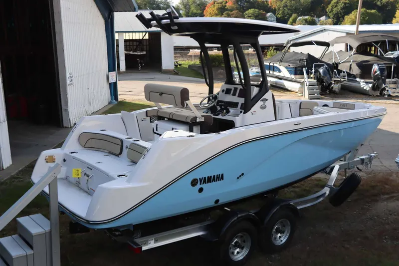 Slide: The Image of 2025 Yamaha Boats 222 FSH Sport E, blue and white, on trailer near boatyard. - 3