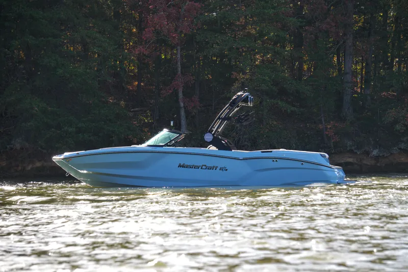 The Image of 2024 MasterCraft NXT23 boat cruising on a lake with forested background. - 0