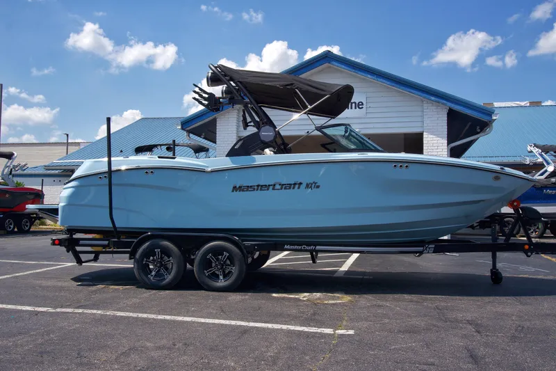 Slide: The Image of 2024 MasterCraft NXT23 boat on trailer, parked outdoors under blue sky. - 6