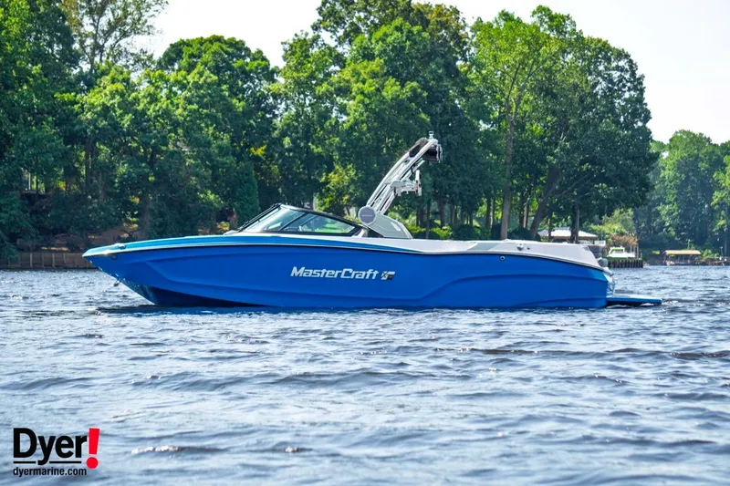 Slide: The Image of 2024 MasterCraft XT24 boat on a lake with lush green trees in the background. - 0