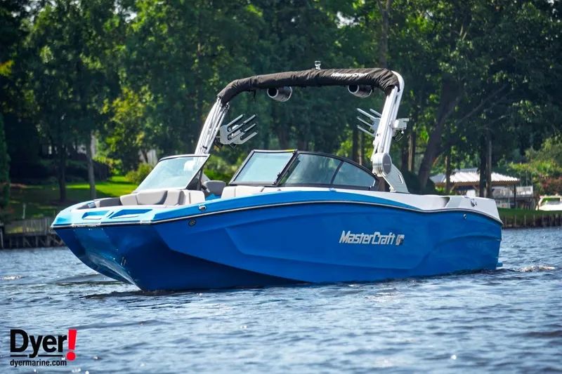 Slide: The Image of 2024 MasterCraft XT24 boat in blue on a lake, surrounded by trees. - 1