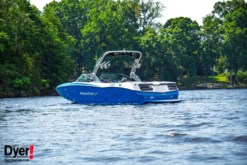Slide: The Image of 2024 MasterCraft XT24 boat on a serene lake with lush green trees. - 2