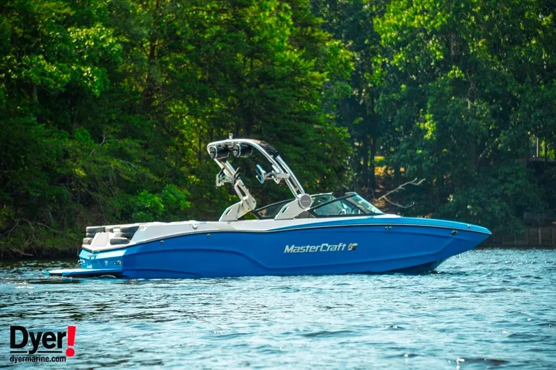 Slide: The Image of 2024 MasterCraft XT24 boat on a serene lake with lush green trees. - 4