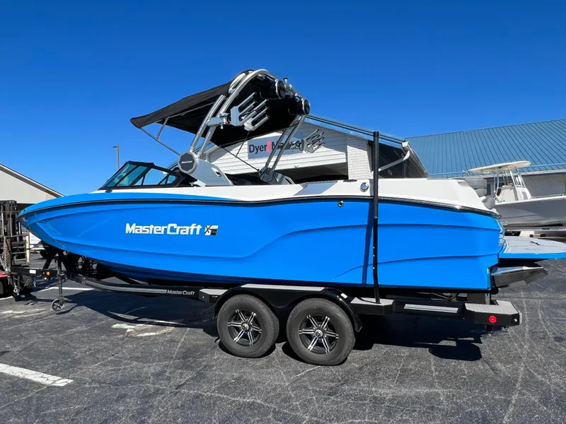 Slide: The Image of 2024 MasterCraft XT24 boat in vibrant blue on a trailer, parked outdoors. - 6