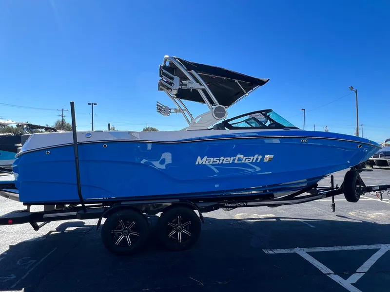Slide: The Image of 2024 MasterCraft XT24 boat in vibrant blue on a trailer under clear skies. - 7