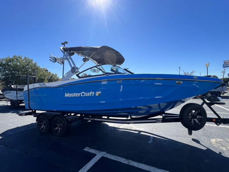 Slide: The Image of 2024 MasterCraft XT24 boat in vibrant blue on a trailer under clear skies. - 8