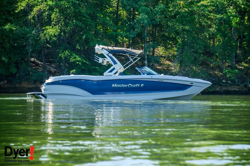 The Image of 2024 MasterCraft X24 boat on a serene lake with lush green forest backdrop. - 0