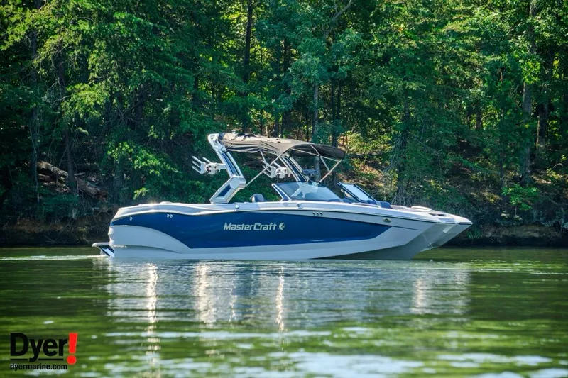 Slide: The Image of 2024 MasterCraft X24 boat on a serene lake with lush green forest backdrop. - 2