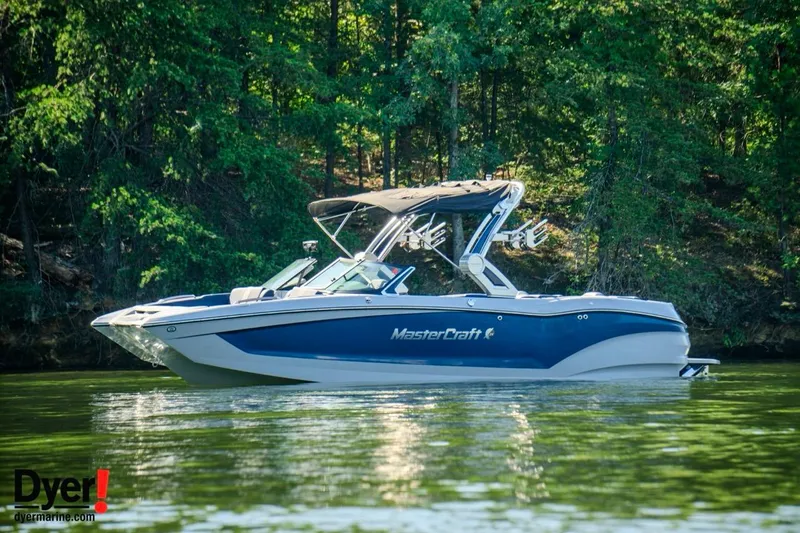 Slide: The Image of 2024 MasterCraft X24 boat on a serene lake with lush forest backdrop. - 6