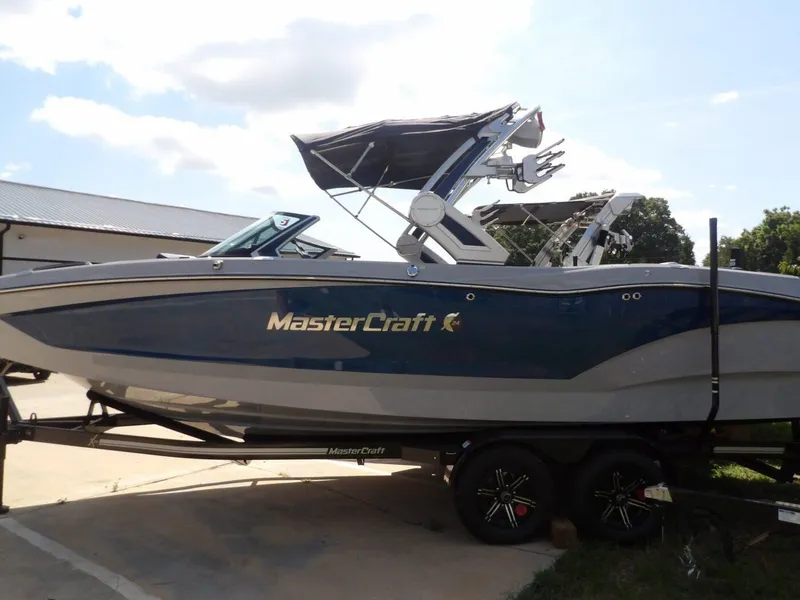 Slide: The Image of 2024 MasterCraft X24 boat on trailer, blue and gray design, parked outdoors. - 7