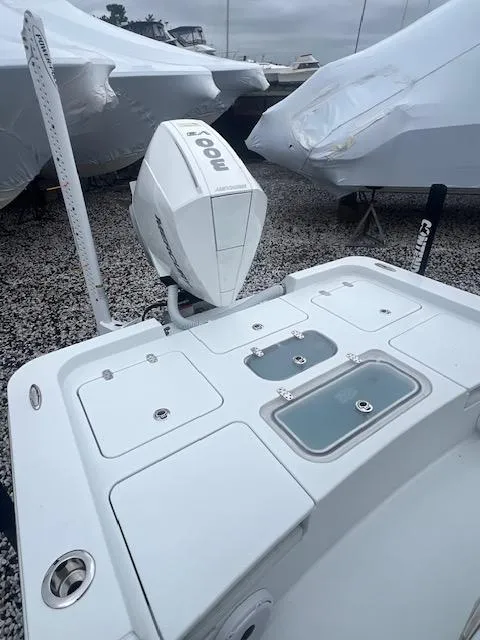 Slide: The Image of 2024 Contender 26 Bay boat with motor, docked on gravel near covered boats. - 2