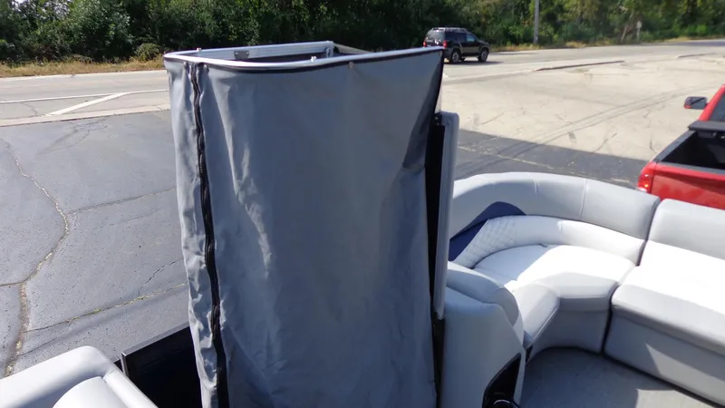 Slide: The Image of 2022 Manitou 23 SES Bench boat with privacy curtain, parked on pavement. - 24