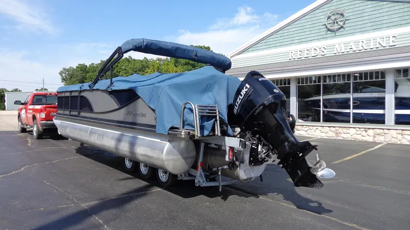 Slide: The Image of 2022 Manitou 23 SES Bench pontoon boat with cover, parked outside a marine store. - 27