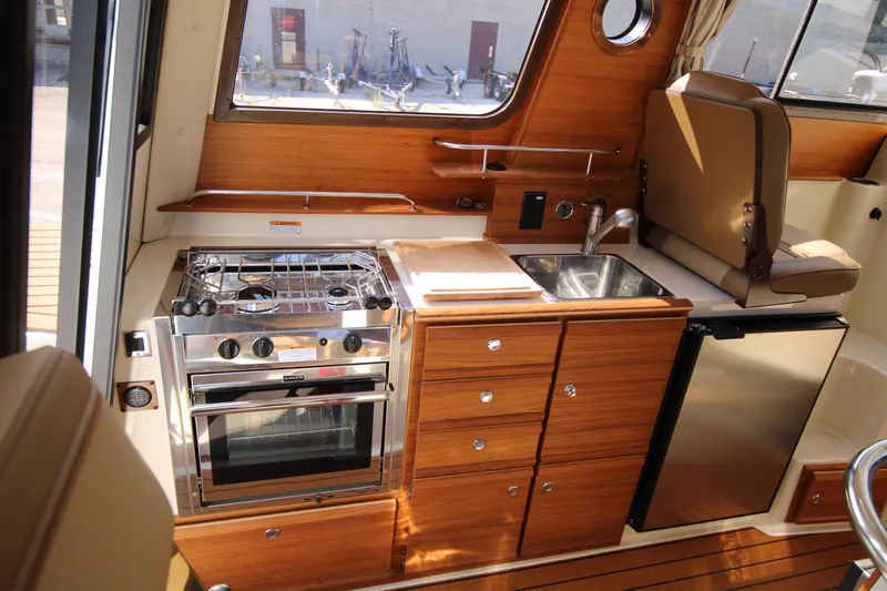 Slide: The Image of 2023 Ranger Tugs R-27 Luxury Edition kitchen with stove, sink, and fridge. - 1