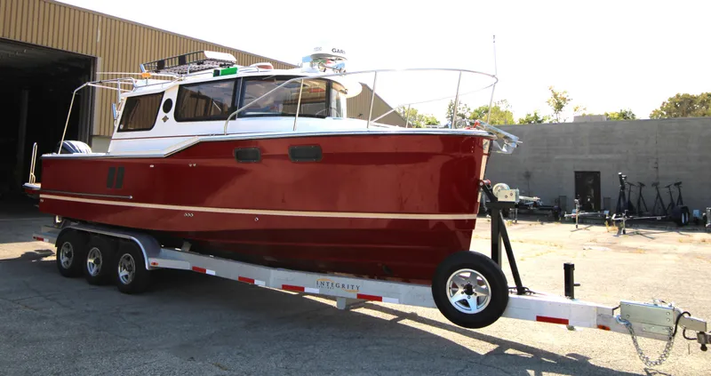 Slide: The Image of 2023 Ranger Tugs R-27 Luxury Edition boat on trailer, red hull, parked outdoors. - 5