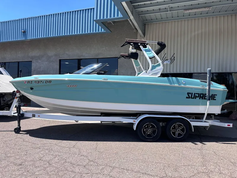 Slide: The Image of 2022 Supreme S220 boat on trailer, parked outside a building. - 1