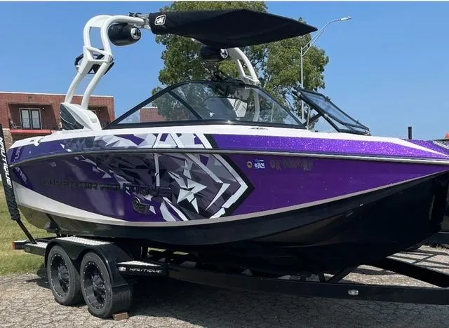 The Image of 2014 Nautique Super Air Nautique G21 boat with purple and white design on trailer. - 0