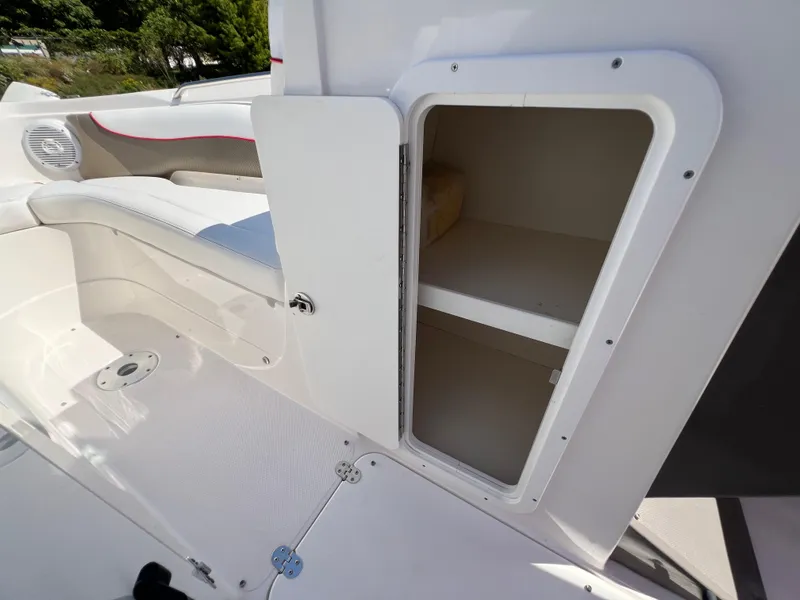 Slide: The Image of 2009 Rinker 246 Captiva Bowrider storage compartment with open door, white interior, and seating area. - 26