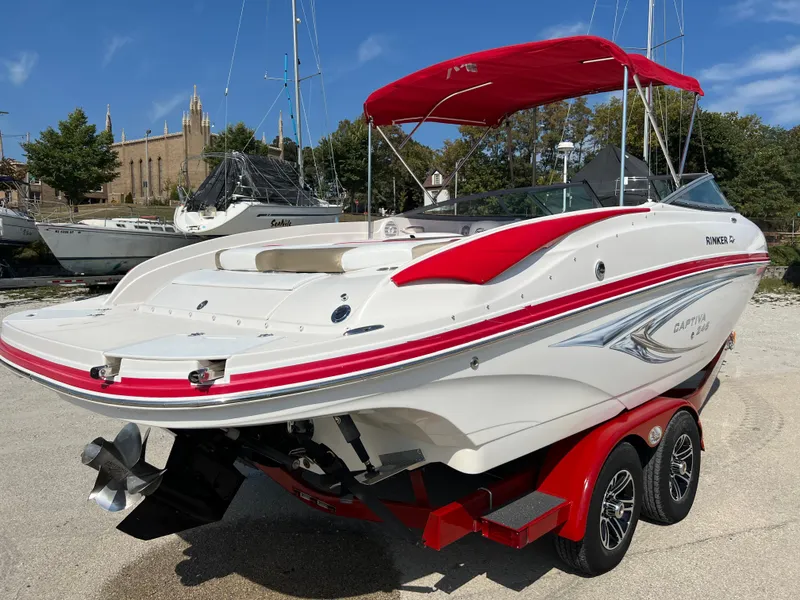 Slide: The Image of 2009 Rinker 246 Captiva Bowrider with red accents on a trailer, docked outdoors. - 9