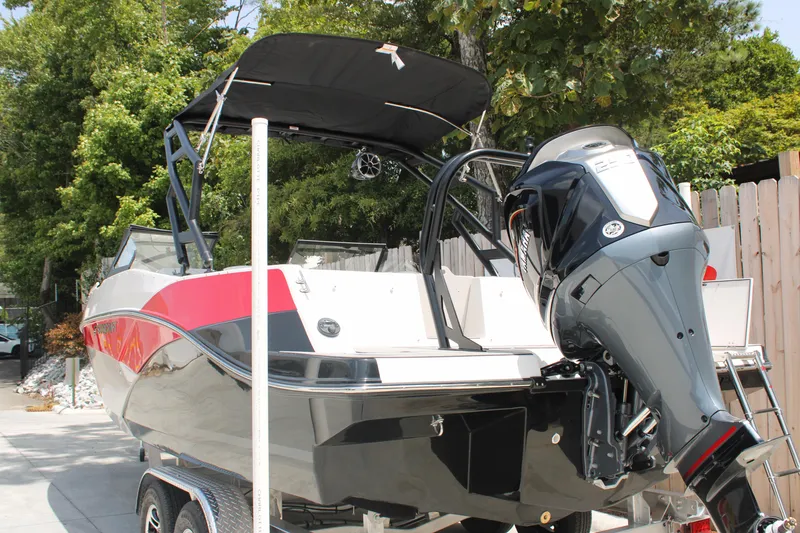 Slide: The Image of 2025 Starcraft 230 boat with outboard motor, parked on trailer, surrounded by trees. - 4