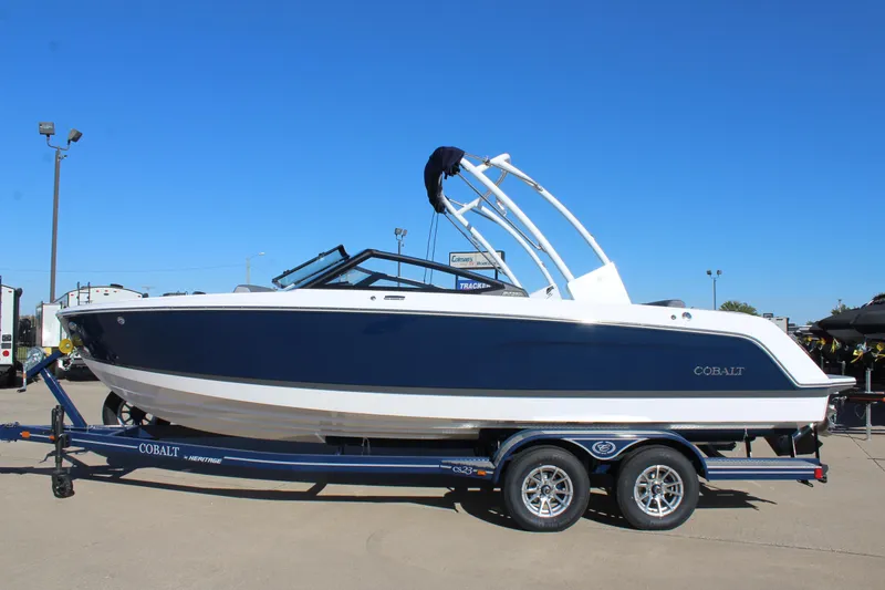The Image of 2025 Cobalt CS23 boat on trailer, blue and white design, parked outdoors. - 0
