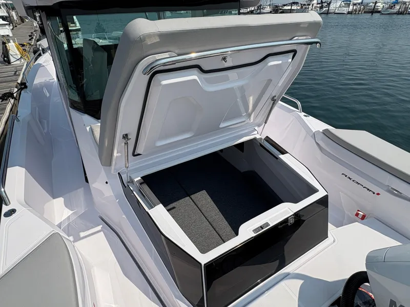 Slide: The Image of 2025 Axopar 29 XC Cross Cabin with open storage compartment, docked by the water. - 11