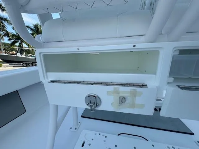 Slide: The Image of 2025 Sportsman Masters 247 Bay Boat interior storage compartment with latch, white seating, and palm trees. - 23