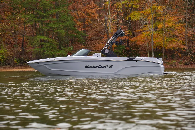 The Image of 2025 MasterCraft XT23 boat on a lake with autumn foliage background. - 0
